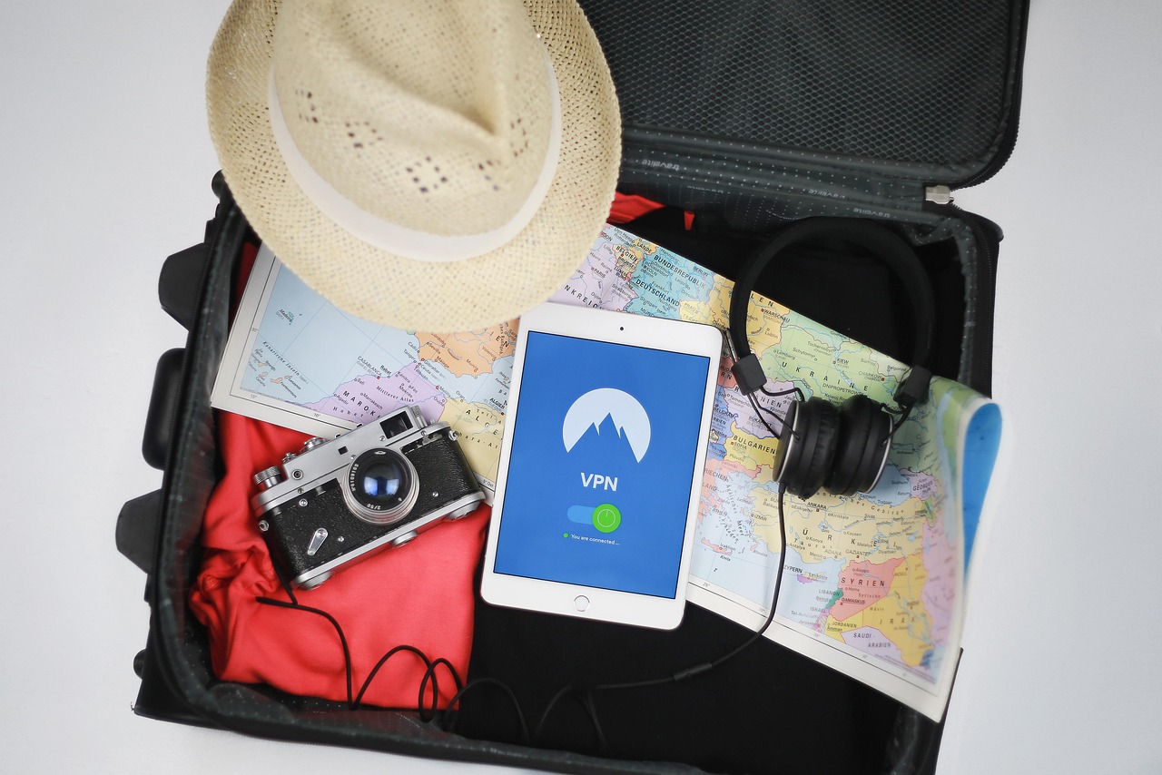 A suitcase with a camera, cell phone, maps, hat and headphones